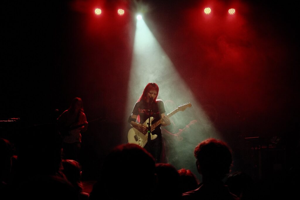 akriila on guitar under a white spotlight and red stage lights