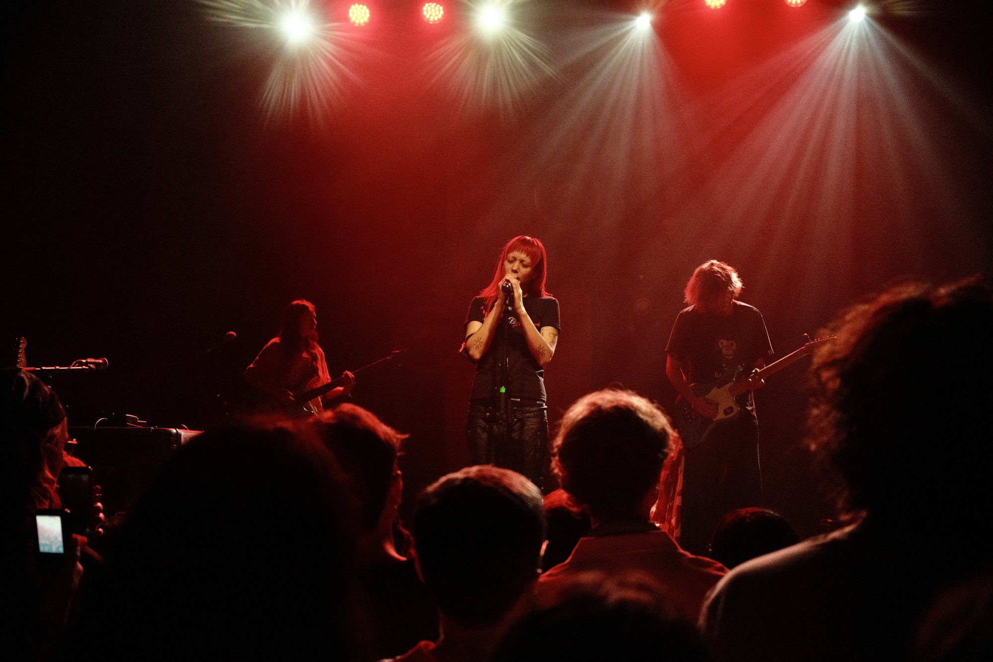 akriila and band in red light, eyes closed at the mic
