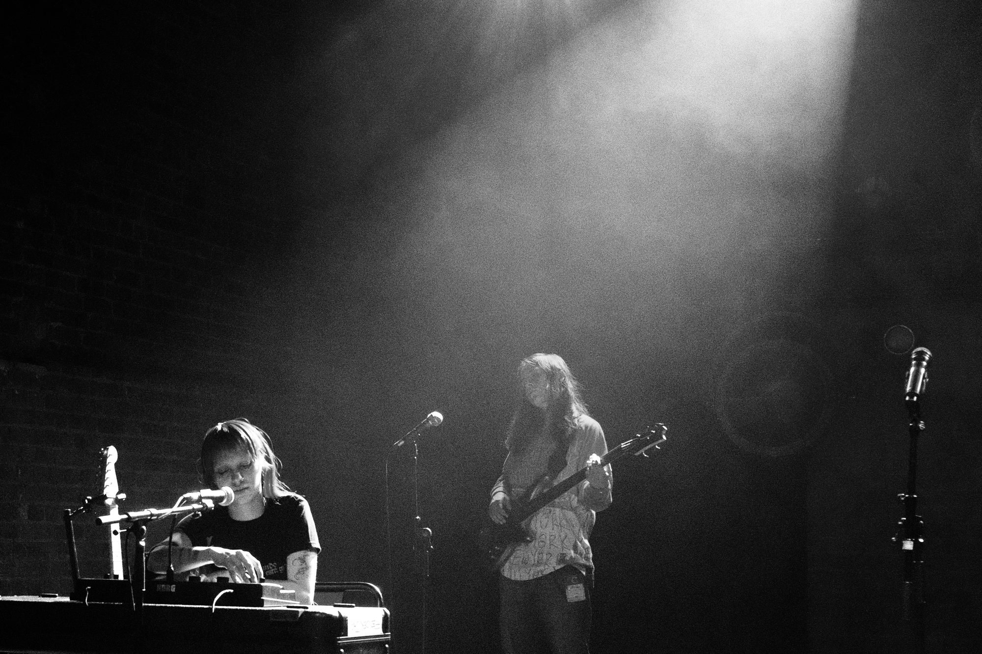 akriila band on keys and bass under a single spotlight, black and white